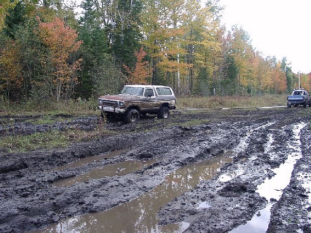 Brown 1978 Ford Bronco stuck in mud with trees in background