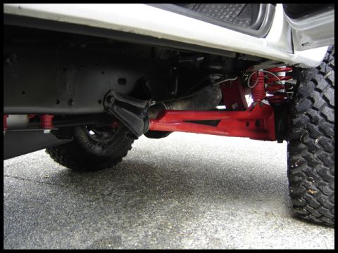 1989 Jeep Cherokee - The underside of a modified vehicle shows red suspension parts and aggressive off-road tires.