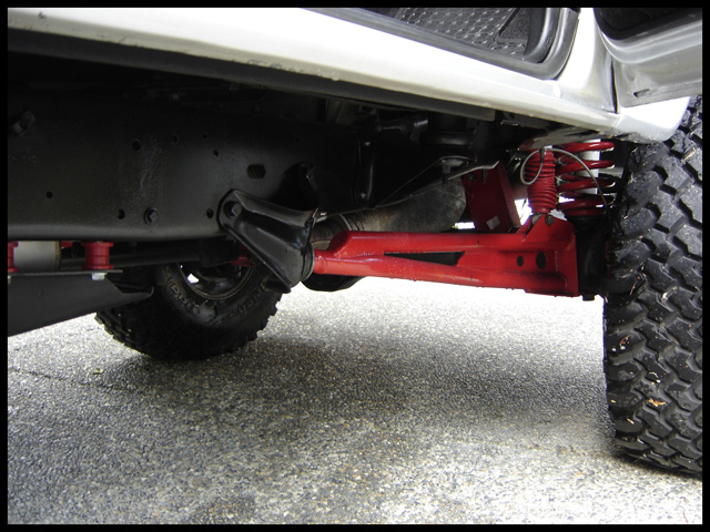 Undercarriage of a lifted vehicle with red suspension components and large tires