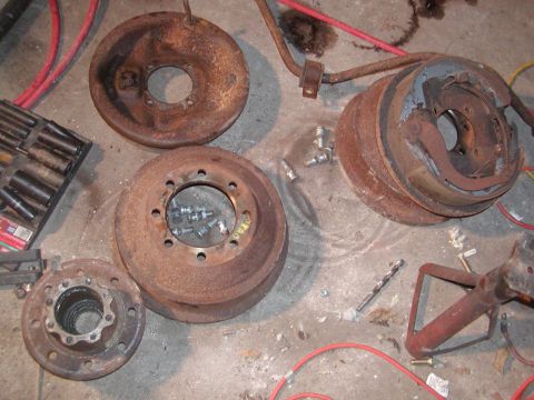 1991 Ford Bronco - Several rusty brake drums and rotors are laid out on a concrete surface, along with some hardware and tools.