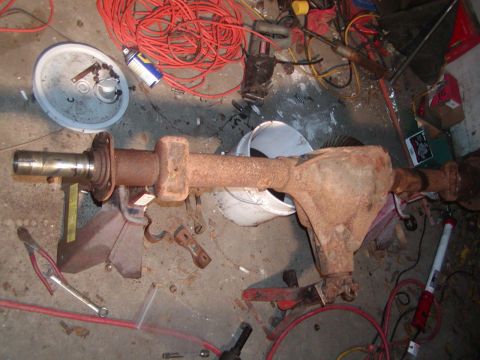1991 Ford Bronco - Rear axle assembly, likely from a truck or SUV, sits on jack stands amidst a cluttered workshop environment.