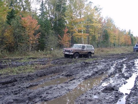 1978 Ford Bronco - A brown 1978 Ford Bronco navigates a muddy trail with trees in the background.