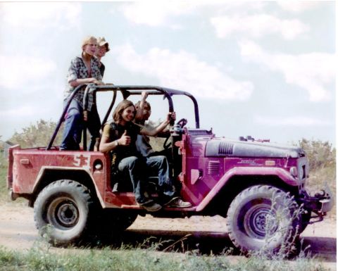 1968 Ford Mustang - Four people enjoy a ride in a vintage Toyota Land Cruiser on a dirt road under a cloudy sky.