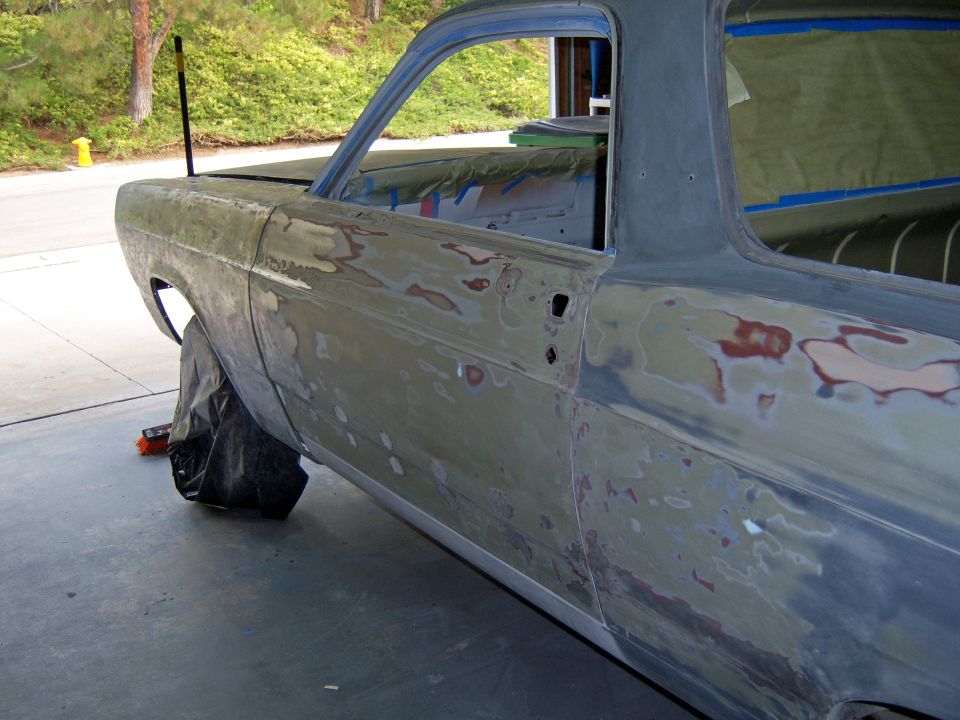 Classic car body in primer with sanded bare-metal spots in a garage