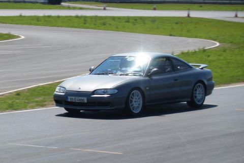 1991 Ford Probe - A dark gray coupe with white wheels navigates a turn on a race track, displaying a 1993 license plate.