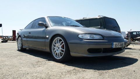 1991 Ford Probe - A gray Mazda MX-6 is parked outdoors next to a dark SUV and a trailer.