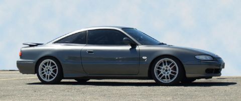 1991 Ford Probe - A gray coupe with a spoiler and aftermarket wheels is parked outdoors under a clear sky.
