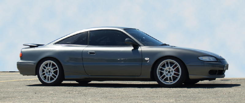 Gray coupe with a rear spoiler and white multi-spoke wheels, seen from the side