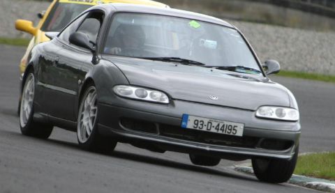 1991 Ford Probe - Mazda MX-6 on a race track with another car following closely behind.