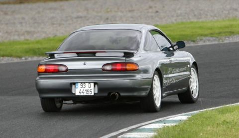 1991 Ford Probe - Gray coupe with white wheels seen from the rear on a race track, displaying a 1993 license plate.
