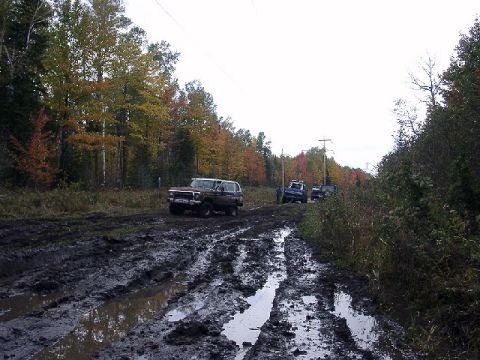 1978 Ford Bronco - Several vehicles navigate a challenging muddy trail during autumn.