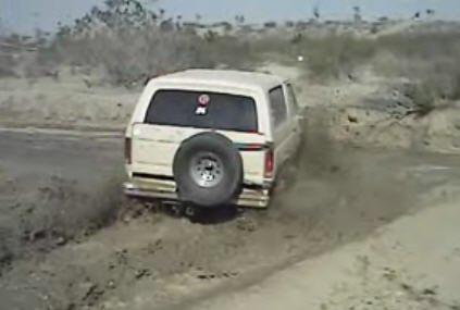1995 Ford Bronco - This 1995 Ford Bronco navigates a muddy terrain, its rear profile and external spare tire.