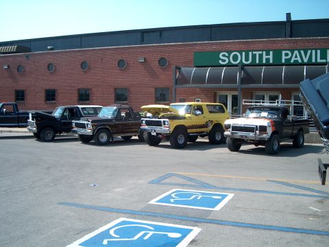 1978 Ford Bronco - Several trucks and a yellow SUV are parked in a lot outside a building labeled "SOUTH PAVILION".