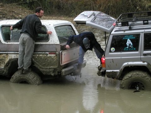 1978 Ford Bronco - Two off-road vehicles are stuck in deep mud, with one person attempting to access the rear of a Ford Bronco.