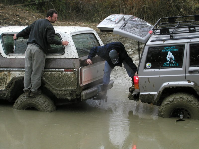 Mud-covered 1978 Ford Bronco with its tailgate open, stuck in deep mud next to a Jeep Cherokee