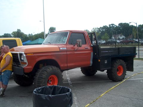 1978 Ford Bronco - This modified Ford truck features a flatbed and oversized tires, with a man standing beside it.