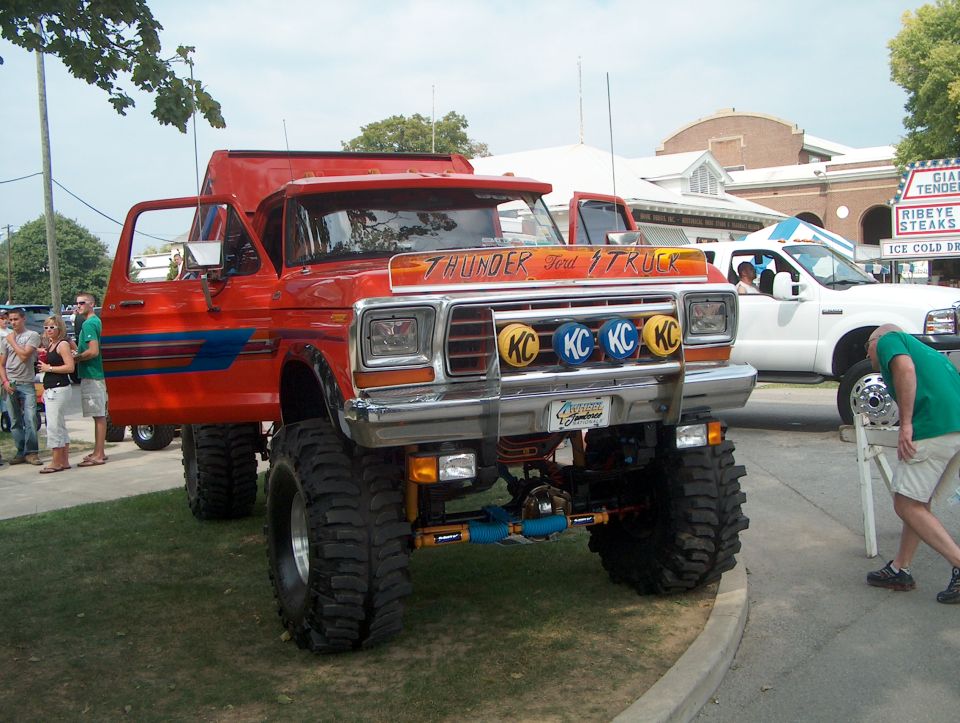 Red lifted 1978 Ford Bronco with "THUNDER FORD TRUCK" on visor, KC lights, and blue racing stripes