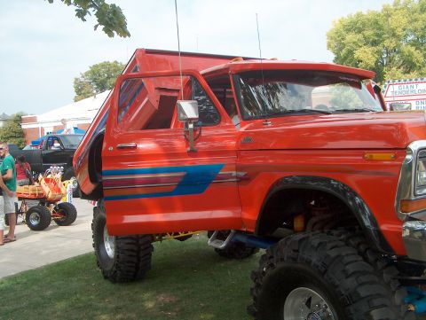 1978 Ford Bronco - Customized orange truck with a dump bed and distinctive stripe graphics, seen at an outdoor event.