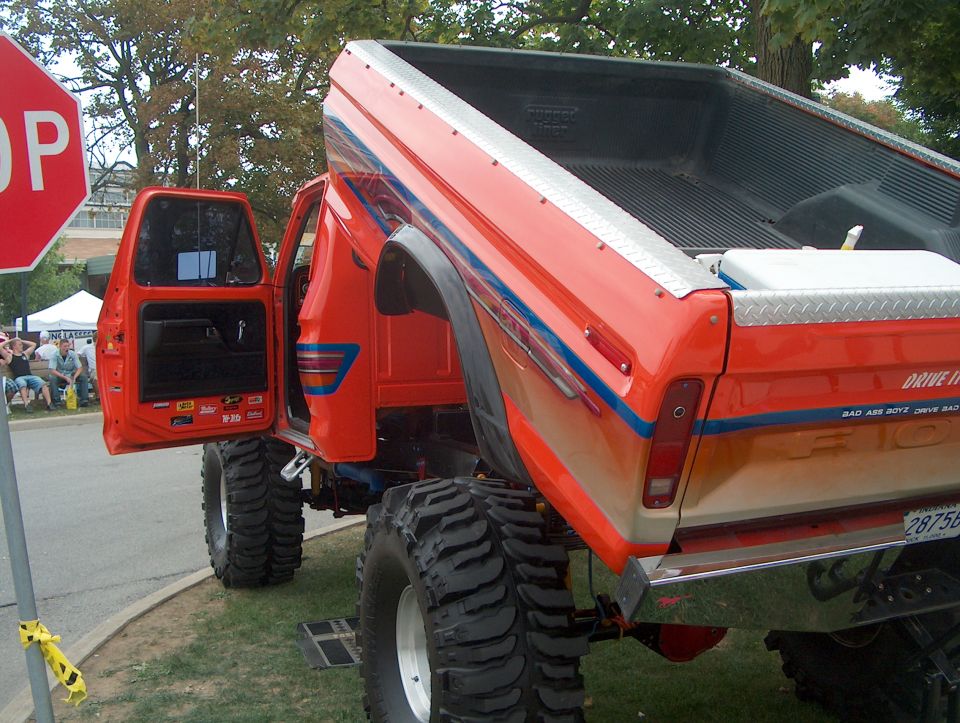 Orange lifted pickup truck with open driver's door, large tires, and custom stripes
