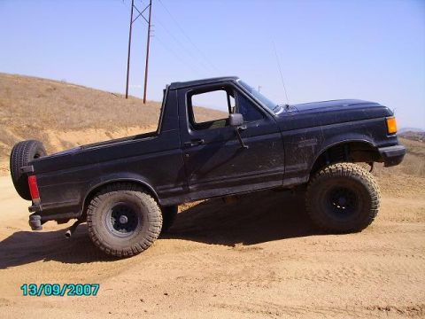 1990 Ford Bronco - A black 1990 Ford Bronco is shown from the side, equipped for off-road use with lifted suspension and large tires.