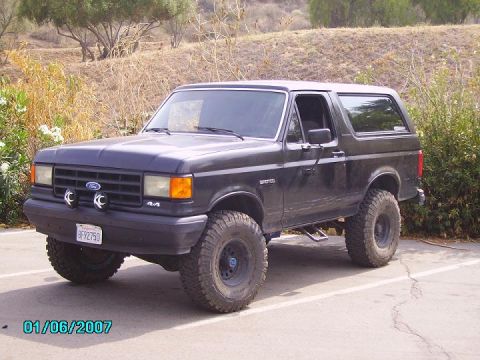 1990 Ford Bronco - This dark-colored Ford Bronco is shown from a three-quarter front angle, off-road tires and a lifted suspension.
