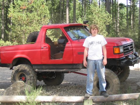1989 Ford Bronco - Red 1989 Ford Bronco parked off-road with a young person standing next to it.