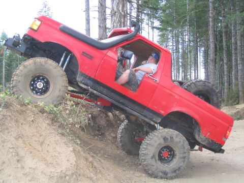 1989 Ford Bronco - A red pickup truck is navigating a steep, muddy incline in a wooded area.