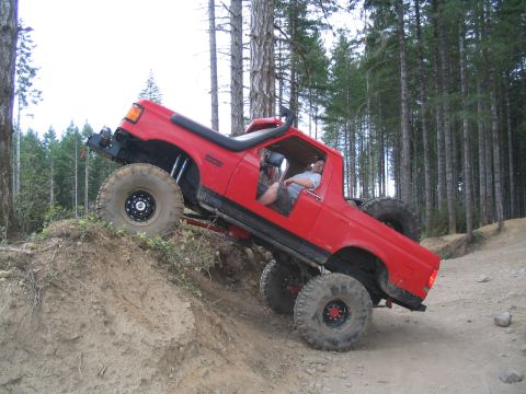 1989 Ford Bronco - A red off-road SUV navigates a steep dirt incline in a wooded area.