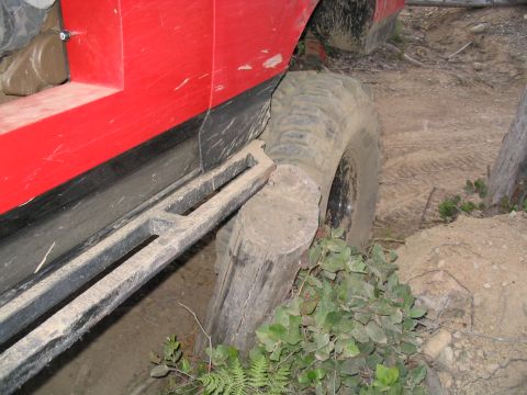 1989 Ford Bronco - A red off-road vehicle navigates a challenging terrain, with its tire pressed against a fallen log.