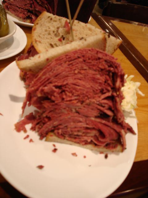 1994 Ford Bronco - A towering pastrami sandwich on rye bread, served with a side of coleslaw, is presented on a white plate.