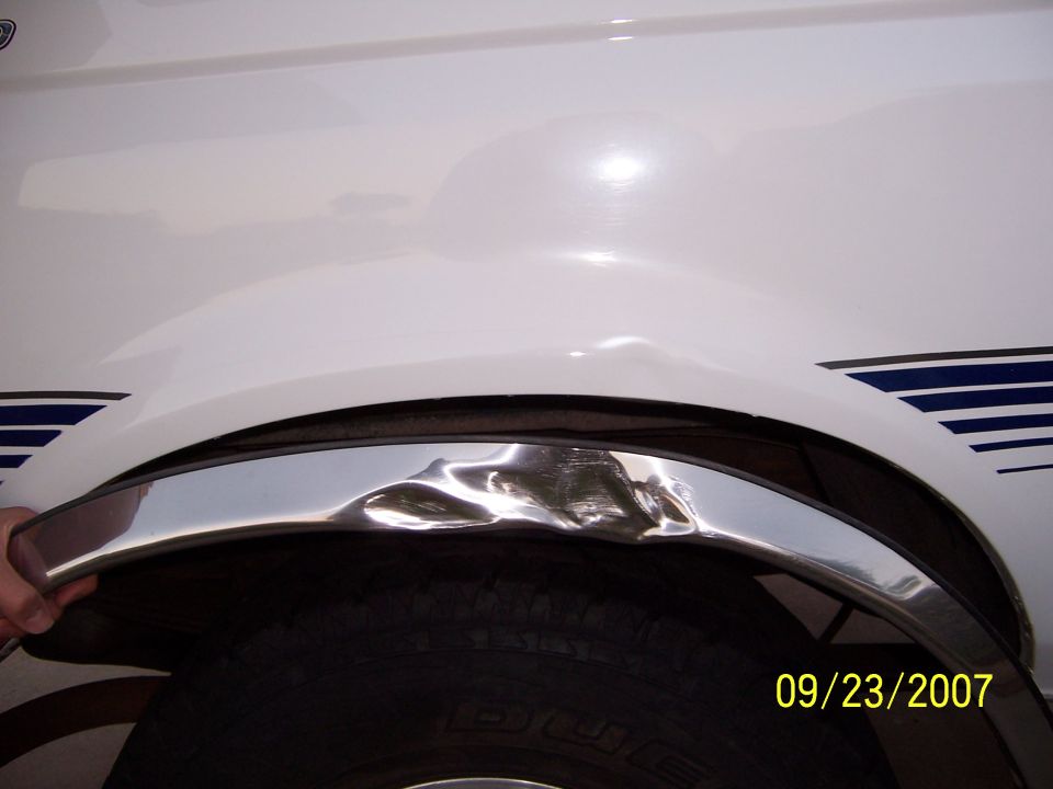 White SUV fender with dented chrome trim and blue stripe detail