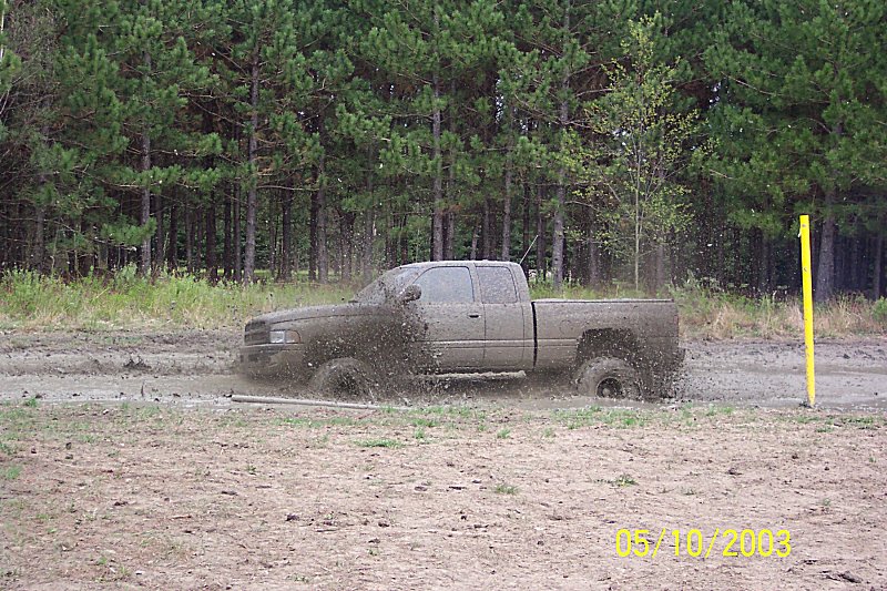 Mud-covered extended-cab pickup splashing through a mud pit in front of pine trees, dated 05/10/2003