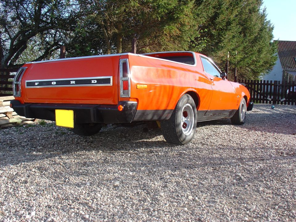 Orange 1974 Ford Ranchero with black bumper and tailgate panel, parked on gravel