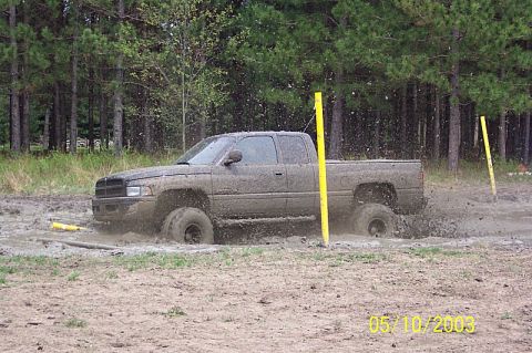1978 Ford Bronco - A pickup truck is stuck in the mud, with trees in the background and water splashing.