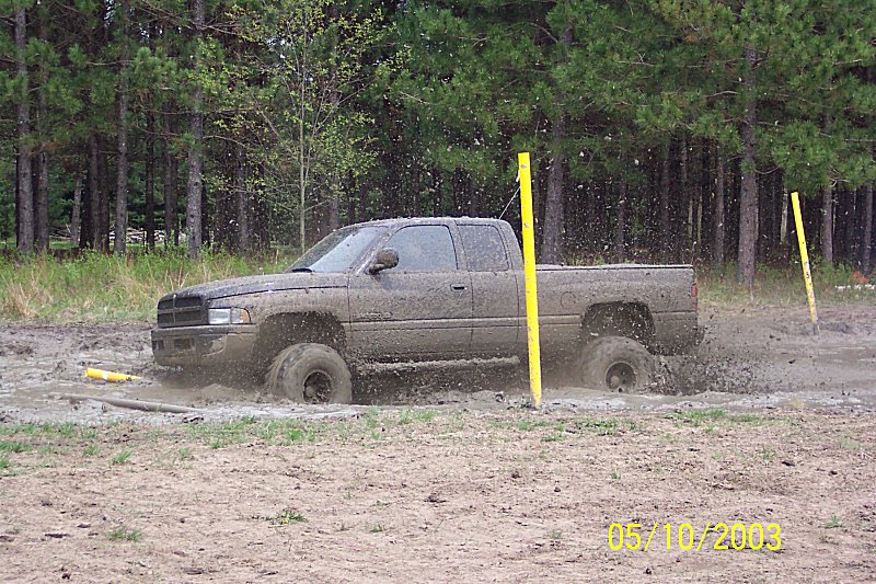 Mud-covered pickup truck stuck in mud with yellow poles nearby