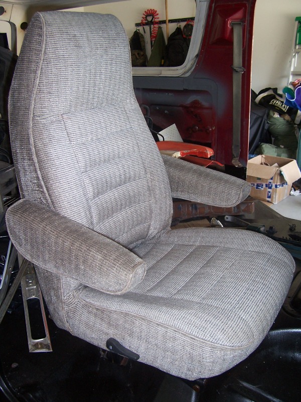 Gray fabric vehicle seat with armrests, inside a vehicle with red interior panels visible