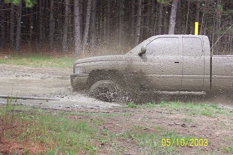 1978 Ford Bronco - A pickup truck navigates a muddy obstacle, sending mud flying in all directions.