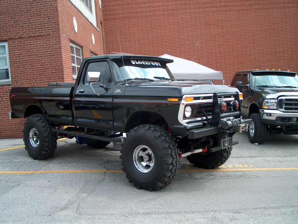 Black pickup truck with large tires and winch, parked next to another truck