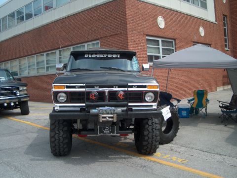 1978 Ford Bronco - A modified black Ford truck with oversized tires and a winch is parked outside a brick building.