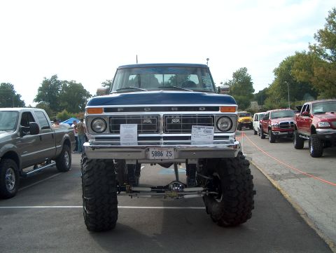 1978 Ford Bronco - Head-on front view of a lifted dark-blue and white late-1970s Ford Bronco at an outdoor show, with FORD lettering across the chrome grille…