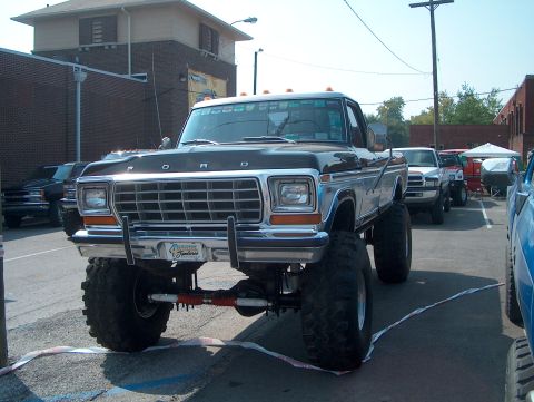 1978 Ford Bronco - A heavily modified Ford F-Series truck is parked in a lot, with other vehicles visible in the background.