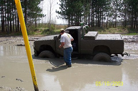 1978 Ford Bronco - Pickup truck is stuck deep in mud with a person standing beside the open driver's door.