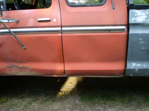 1979 Ford Bronco - Side view of an orange truck door and fender showing chrome trim and signs of rust.