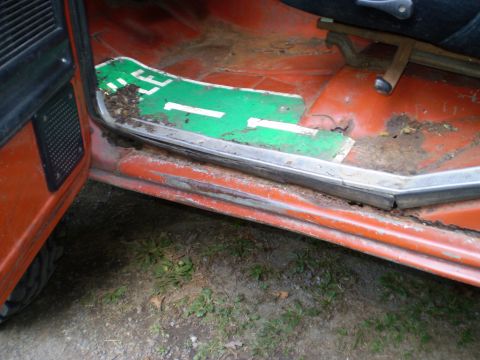 1979 Ford Bronco - Interior view of a vehicle's door sill, showing rust and a green mat with white markings.