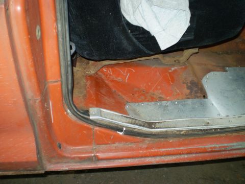 1979 Ford Bronco - Interior view of an orange vehicle's door jamb, revealing worn floor panels and a black seat.