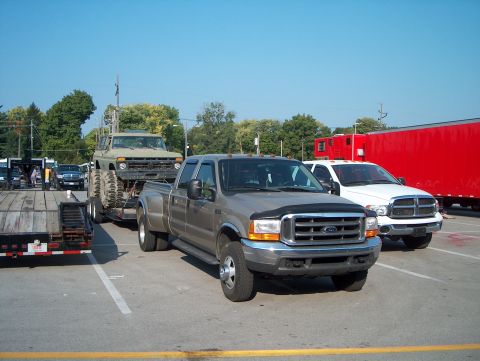 1978 Ford Bronco - A Ford F-350 tows a heavily modified Jeep on a trailer, with other vehicles and a red trailer in the background.