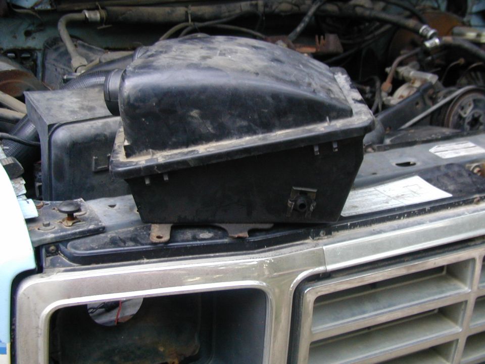 Dusty black air cleaner housing on top of a chrome grille. Engine components visible behind