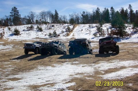 1978 Ford Bronco - Multiple off-road vehicles navigate a snowy and sandy landscape under a clear blue sky.