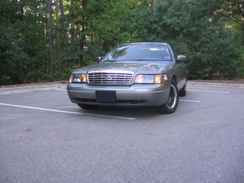 2000 Ford Crown Victoria - A gray 2000 Ford Crown Victoria is parked in an outdoor lot with trees in the background.