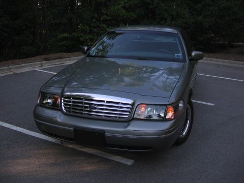 2000 Ford Crown Victoria - A silver 2000 Ford Crown Victoria is parked in a lot with trees in the background.